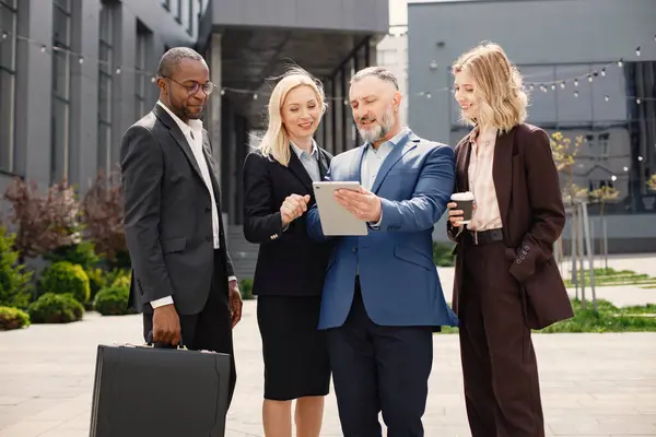 Modern ofis binasının önünde duran kendinden emin iş adamları. Erkekler ve kadınlar konuşuyorlar ve belgelere bakıyorlar. Bankacılık ve finans piyasası kavramı.