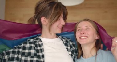 Bir çift genç lezbiyen kız gökkuşağı bayrağına karşı ve mutlu bir şekilde sarılıyorlar. Bir çift lezbiyen kadın..