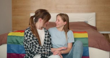 Bir çift genç lezbiyen kız gökkuşağı bayrağına karşı ve mutlu bir şekilde sarılıyorlar. Bir çift lezbiyen kadın..