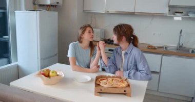 Pizza yiyip mutfakta oturan iki mutlu genç kız. Lgbtq çifti birlikte yaşıyor..