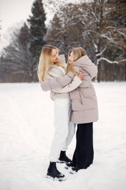 Anne ve kızı kar tatilinde ormanda eğleniyorlar. Bej rengi ceketli bir aile. Kadın ve genç kız sarılıyor..