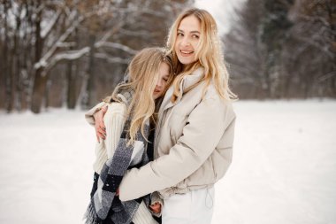 Anne ve kızı kar tatilinde ormanda eğleniyorlar. Bej ceketli bir kadın ve ekose battaniyeye sarılmış bir kız. Kadın ve genç kız sarılıyor..