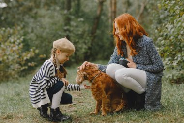 Anne ve kızı köpekle oynuyorlar. Sonbahar parkında bir aile. Evcil hayvan ve yaşam tarzı konsepti. Sonbahar zamanı.