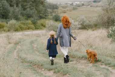 Anne ve kızı köpekle oynuyorlar. Sonbahar parkında bir aile. Evcil hayvan ve yaşam tarzı konsepti. Sonbahar zamanı.