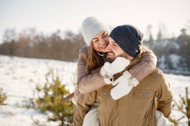 Kış yürüyüşünde eğlenen romantik çift portresi. Kadını sırtında taşıyan bir adam. Aile ceketi ve örgü şapkalar giyiyor..