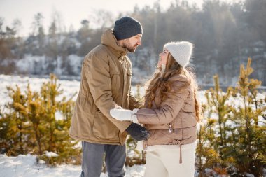 Kış yürüyüşünde eğlenen romantik çift portresi. Erkek ve kadın el ele tutuşuyor. Aile ceketi ve örgü şapkalar giyiyor..