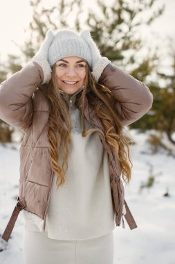 Genç sarışın kadın kışın doğa üzerinde duruyor. Fotoğraf için poz veren bir kız. Kahverengi ceketli, gri şapkalı ve eldivenli kadın..