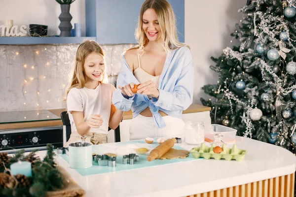 Family preparation of ginger biscuits with daughter. Mother and little girl break an egg. Blonde woman wearing blue shirt and girl white t-shirt.