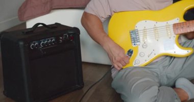 Oturma odasında gitar çalan genç bir adam. Yükseltici ayarlanıyor.