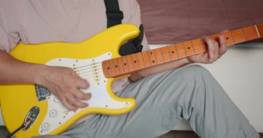 Oturma odasında gitar çalan genç bir adam. Yükseltici ayarlanıyor.