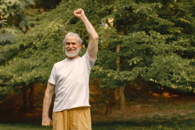 Beyaz tişörtlü son sınıf öğrencisi parkta duruyor ve antrenman yapıyor. Olumlu olgun kadınlarda fitness ya da yoga dersi vardır. Emeklilikte sağlık ve sağlıklı yaşam tarzı.