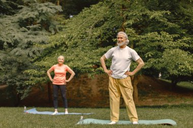 Park yerinde yoga minderleri olan son sınıf erkek ve kadın. Olgun bir adam ve yaşlı eşinin spor ya da yoga dersleri var. Emeklilikte sağlık ve sağlıklı yaşam tarzı.