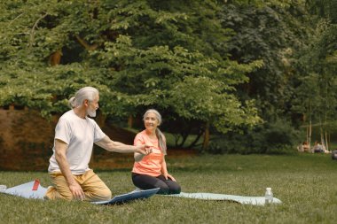 Park yerinde yoga minderleri olan son sınıf erkek ve kadın. Olgun bir adam ve yaşlı eşinin spor ya da yoga dersleri var. Emeklilikte sağlık ve sağlıklı yaşam tarzı.