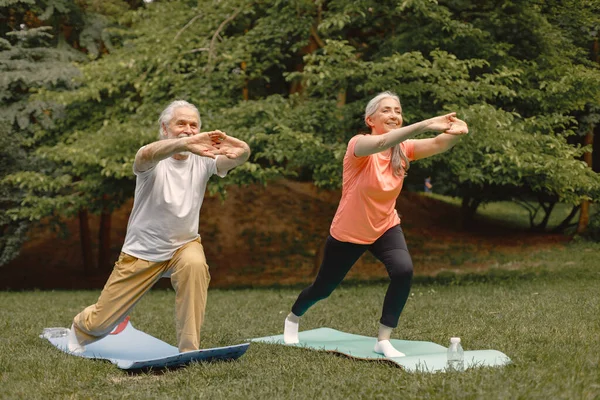 Senior man and woman with yoga mats standing at park. Positive mature man and his elderly wife have a fitness or yoga class in nature. Wellness and healthy lifestyle on retirement.