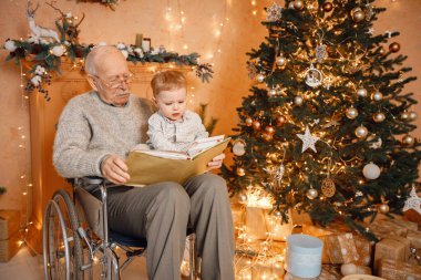 Küçük çocuk ve büyükbabası Noel 'i birlikte kutluyorlar. Sarışın torun ve tekerlekli sandalyede Noel ağacının yanında oturan yaşlı dede. Çocuk ve büyükbaba kitap okuyor..