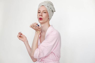 Makyajlı genç bir adam manikür yapıyor. Pembe sabahlık giyen ve kafasında havlu olan bir adam. Beyaz arkaplanda izole edilmiş adam.