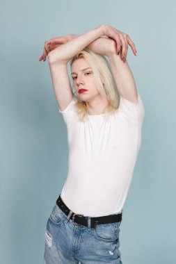 Makyajlı genç sarışın bir adam fotoğraf için poz veriyor. Beyaz tişörtlü ve kırmızı dudaklı bir adam. Mavi arkaplanda izole edilmiş bir adam.