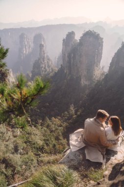 Çin 'deki Zhangjiajie Ulusal Orman Parkı' nda bir kayanın üzerinde oturmuş el ele tutuşan yeni nişanlı çift.