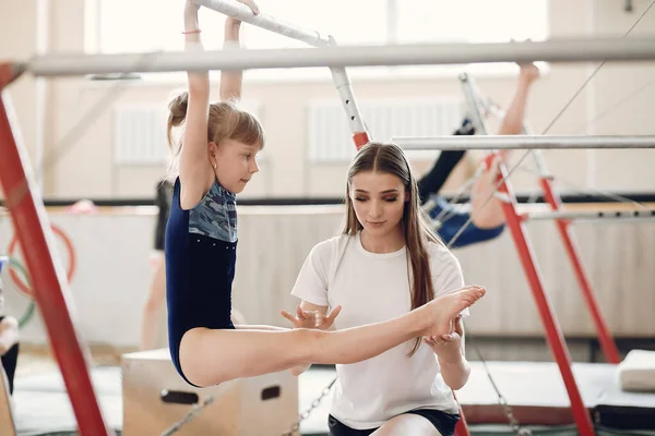 Child gymnastics balance beam. Girl gymnast athlete during an exercise horizontal bar in gymnastics competitions. Coach with child.