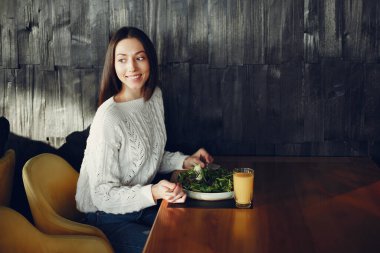 Kız sebze salatası yiyor. Bir kafede oturan bir bayan. Beyaz kazak esmer.