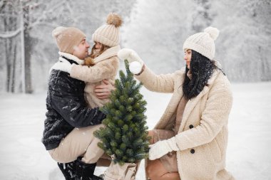 Küçük kız, baba ve anne bir saksıda küçük bir Noel ağacı taşıyor. Esmer genç bir kadın, kışın sıcak ceketli bir adam ve küçük bir kız parkta yürüyorlar. Anne ve kızı kışlık giysiler giyiyor.