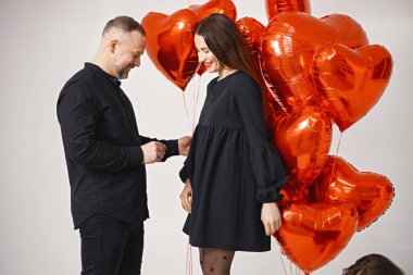 Bir adam kız arkadaşına evlenme teklif ederken fotoğraf için poz veriyor. Stüdyoda, elinde nişan yüzüğü olan bir adamın kalp şeklindeki kırmızı balonların yanında durduğu uzun bir çekim. Esmer kadın ve...