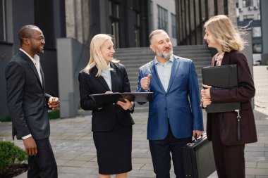Modern ofis binasının önünde duran kendinden emin iş adamları. Erkekler ve kadınlar ellerinde belgelerle konuşuyor. Bankacılık ve finans piyasası kavramı.