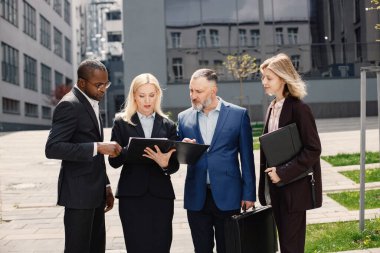 Modern ofis binasının önünde duran kendinden emin iş adamları. Erkekler ve kadınlar ellerinde belgelerle konuşuyor. Bankacılık ve finans piyasası kavramı.