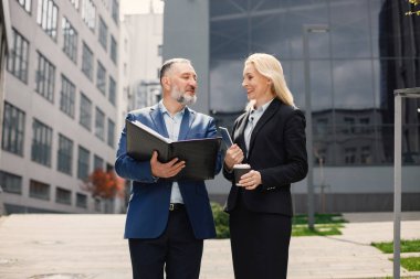 Modern ofis binasının önünde duran kendinden emin iş adamları. Kadın ve erkek konuşuyor ve belgelere bakıyor. Bankacılık ve finans piyasası kavramı.