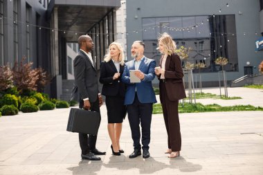 Modern ofis binasının önünde duran kendinden emin iş adamları. Erkekler ve kadınlar konuşuyorlar ve belgelere bakıyorlar. Bankacılık ve finans piyasası kavramı.