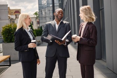Modern ofis binasının önünde duran kendinden emin iş adamları. Siyahi adam ve beyaz kadın konuşuyorlar ve belgelere bakıyorlar. Bankacılık ve finans piyasası kavramı.