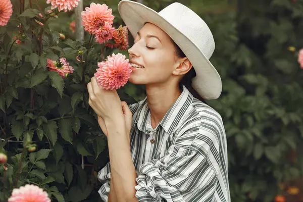 Young woman with pink flowers. Lady in a hat. Girl in a garden.