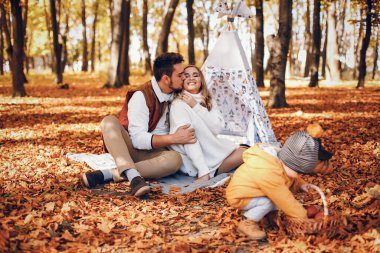 Aile sonbahar parkında eğlenir. Beyaz kazak içinde şirin bir hava kabarcığı. Küçük oğlu olan ebeveynler. Aile çadırın yanında oturuyor..