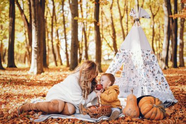 Aile sonbahar parkında eğlenir. Beyaz kazak içinde şirin bir hava kabarcığı. Anne ve küçük oğlu.