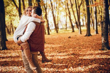 Çiftler sonbahar parkında eğleniyor. Beyaz kazak içinde şirin bir hava kabarcığı..