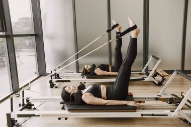 Two young fit women training in gym. Women wearing black sportwear. Caucasian girls excercising with equipment.