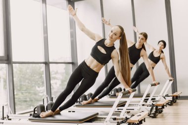 Three young fit women training in gym. Women wearing black sportwears. Caucasian girls excercising with equipment.