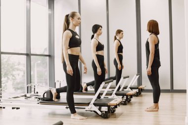 Three young fit women training in gym. Women wearing black sportwears. Caucasian girls excercising with equipment.
