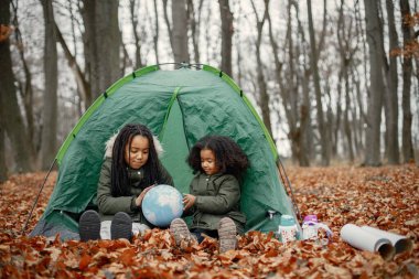Ormanda kamp yapan güzel siyah kızlar. Sonbahar ormanında bir çadırda oturan ve bir küreye bakan iki küçük kız kardeş. Hakiki ceket giyen siyah kızlar..