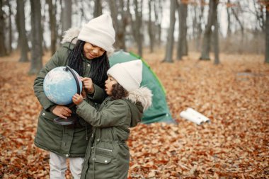 Güz ormanında çadırın yanında duran güzel siyah kızlar. İki küçük kız kardeş bir eldeki küreyi tutuyor. Hakiki ceket giyen siyah kızlar..