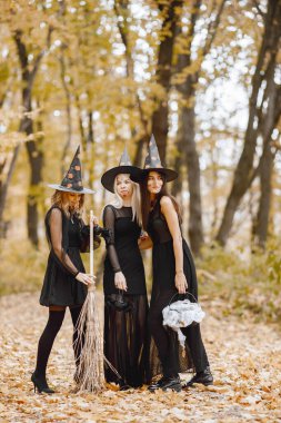 Three young girls witches in forest on Halloween. Girls wearing in black dresses and cone hat. Witch holding a magician stuff.