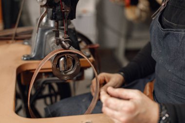 Yetişkin bir zanaatkârın çalışma alanında çekilmiş bir fotoğrafı. Önlük takan ve dikiş makinesi kullanan bir adam. Koyu taş doku arkaplanını öğüt.