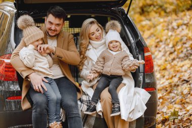 Happy family resting after day spending outdoor in autumn park. Father, mother and two children sitting inside car trunk, smiling. Family holiday and traveling concept.