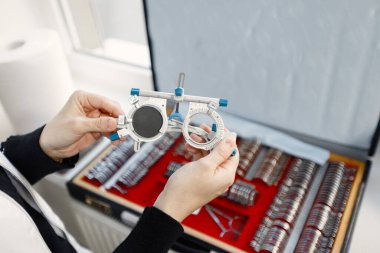 Optometrist, görüş testi ve deneme çerçevesi için göz hekimi deney lensleri hazırlıyor. Optometrik enstrümanlı kadın masası açık. Optometrist beyaz sağlık önlüğü giyiyor.
