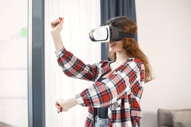 Sanal gerçeklik gözlüğü takan beyaz bir kadın koça yakın duruyor. Ekose gömlek ve kot pantolon giyen bir kız. Kız yalnız zaman geçiriyor..