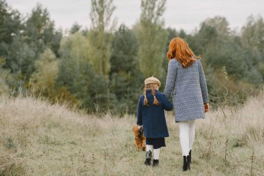 Anne ve kızı köpekle oynuyorlar. Sonbahar parkında bir aile. Evcil hayvan ve yaşam tarzı konsepti. Sonbahar zamanı.
