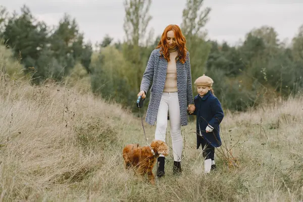 Anne ve kızı köpekle oynuyorlar. Sonbahar parkında bir aile. Evcil hayvan ve yaşam tarzı konsepti. Sonbahar zamanı.