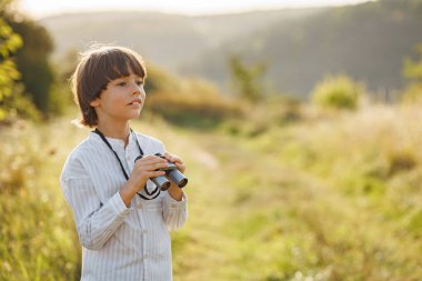 Tarlada dürbünü olan küçük bir kâşifin portresi. Yazın tarlada dürbünden bakan beyaz bir çocuk. Esmer çocuk çizgili gömlek giyiyor..