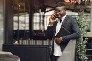 African man. Guy in a black suit. Male with a mobile phone. Businessman at the office.