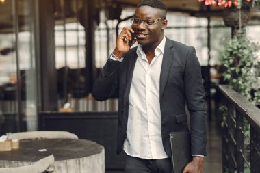 African man. Guy in a black suit. Male with a mobile phone. Businessman at the office.